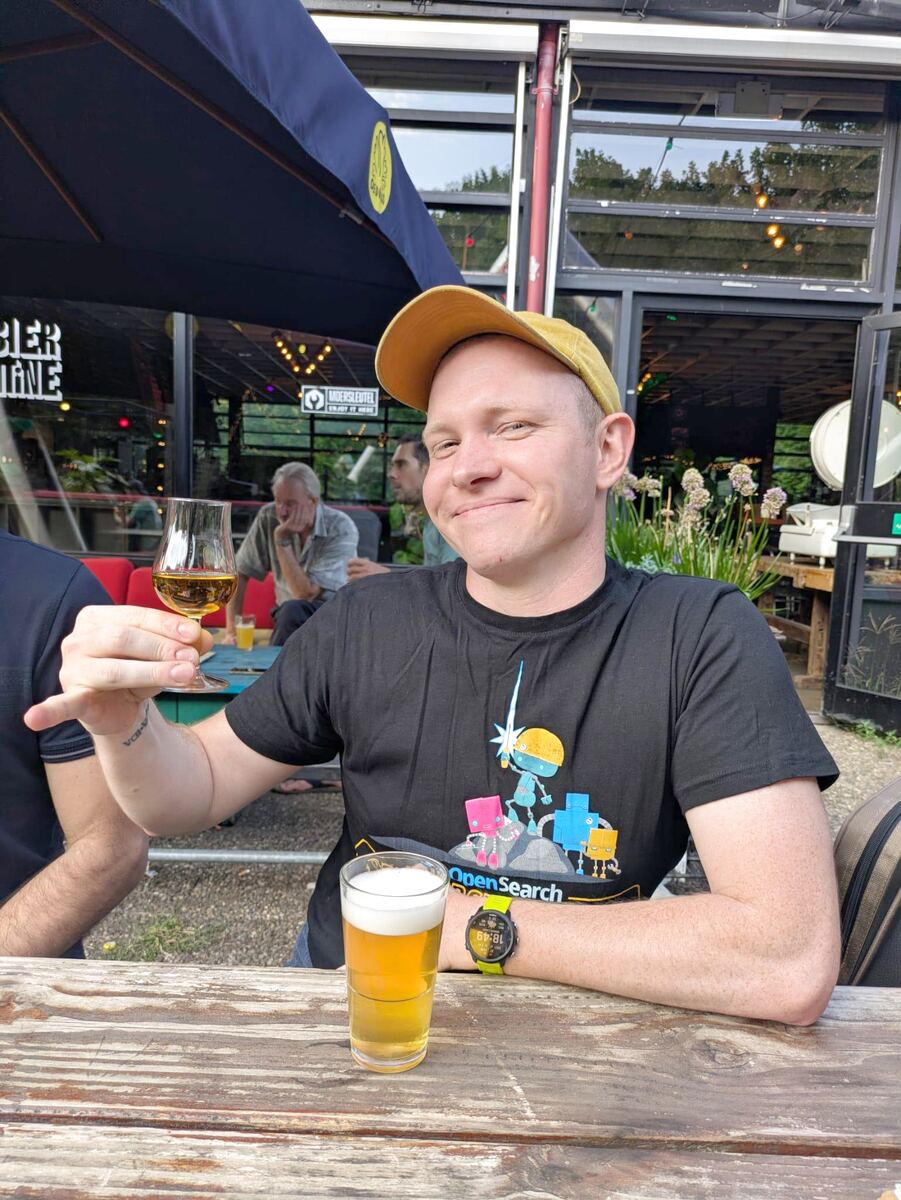 Nandi at a beer garden table, raising a glass with a pint on the table