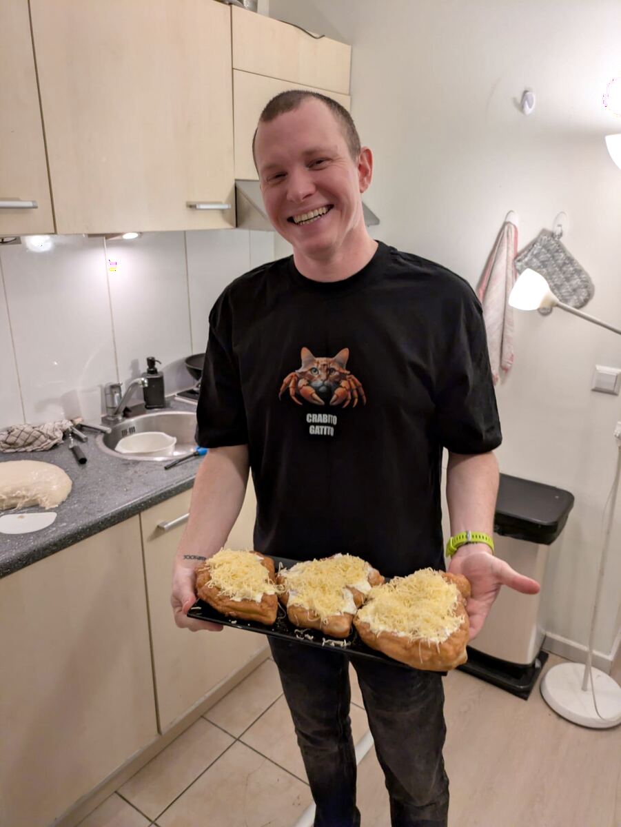 Nandi in a kitchen holding a tray of fresh lángos topped with cheese